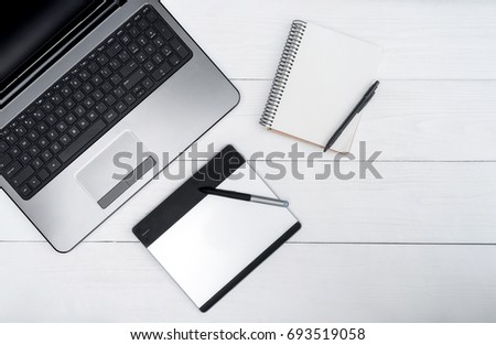 Top view on white wooden table with open blank laptop computer, empty diary and graphic tablet, free space
