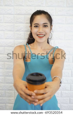 Hot drink in paper cup in hands close up. Cheerful business woman  holding coffee outdoors on white brick  background