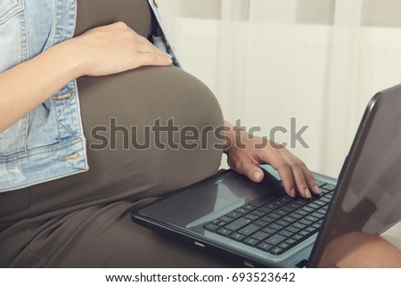 Pregnant woman sitting with laptop on window background