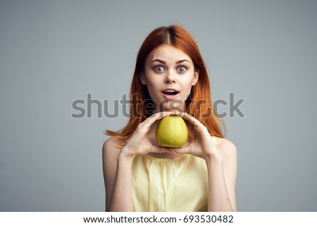 Young beautiful woman on a gray background holds an apple, emotions.