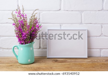 White frame mockup with maroon purple field flowers in polka dot mint green pitcher vase. Empty frame mock up for presentation artwork. Template framing for modern art.