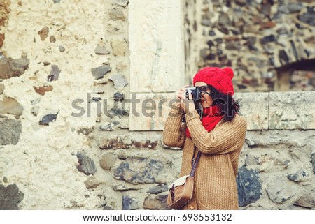 Beautiful young woman taking photos with retro camera on the background of the old stones wall. Lifestyle and tourism concept.