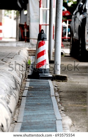 Traffic cones with red and white stripes put on metal grating next to car park.