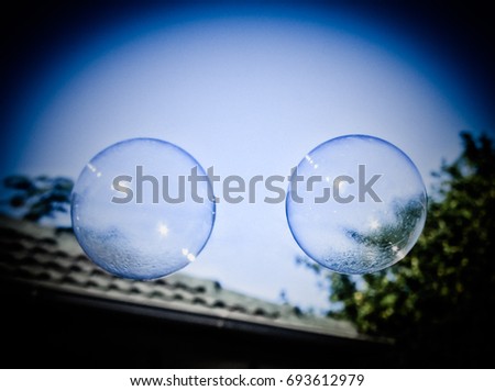 A photograph of a couple of freshly blown bubbles floating through a backyard with a dark vignette border.  This photo was taken in Brisbane, Australia. 