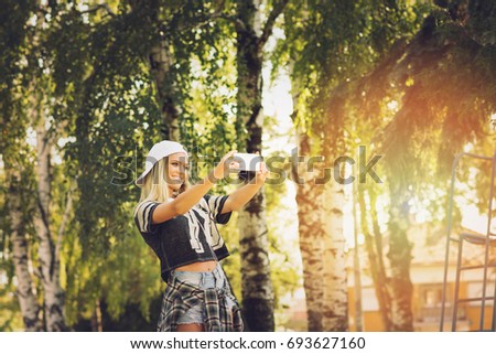 Sporty teenage girl taking a selfie on smart phone in park. Young woman smiling taking a photo of herself outside on sunny day. Vibrant colors, medium retouch.