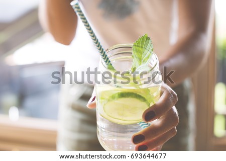 Woman holding glass of infused water with cucumber, lime and mint Royalty-Free Stock Photo #693644677