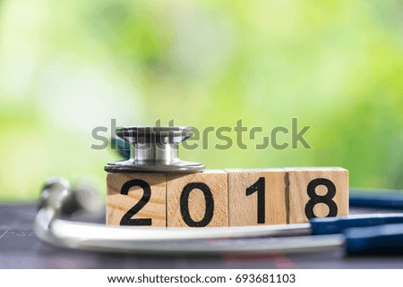 Stethoscope with 2018 wooden text block on world map, health care concept.