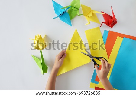 Children's hands do origami from colored paper on white background Royalty-Free Stock Photo #693726835