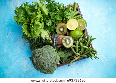 Green vegetables background. Fresh garden produce. Broccoli, spinach, kiwi, lettuce, parsley, dill, asparagus beans, lime on blue concrete background, top view and copy space
