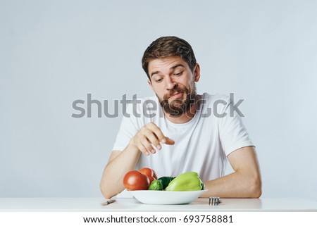 Man with a beard on a light background at a table, vegetables, diet, vegetarianism.