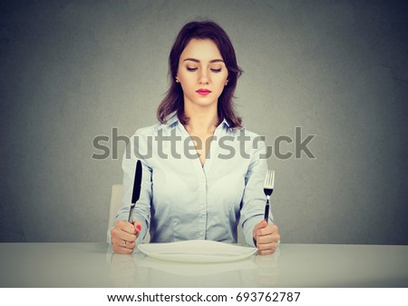 Serious woman with fork and knife sitting at table with empty plate isolated on gray wall background  Royalty-Free Stock Photo #693762787