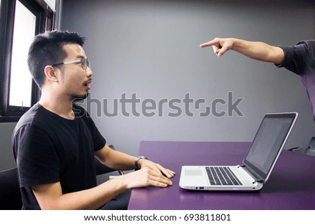 A boss pointing at young man who is working at the office. Grey background.