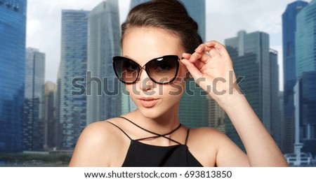 accessories, fashion, people and luxury concept - beautiful young woman in elegant black sunglasses over singapore city skyscrapers background