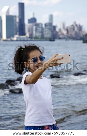 Cute girl taking a self photo. New York City skyline, view from Brooklyn. Waterfront. 