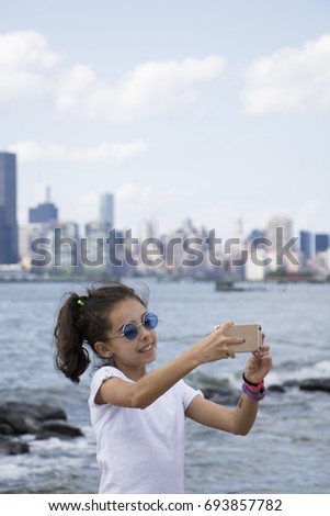 Cute girl taking a self photo. New York City skyline, view from Brooklyn. Waterfront. 