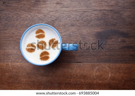 A rustic mug with coffee cream. Food art creative concept image, drawing with cinnamon powder over wooden background.
