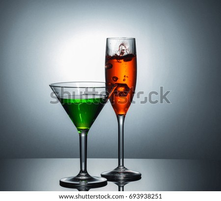 view of  MARTINI and TULIP CHAMPAGNE  GLASS getting splash by ice cube on reflection floor