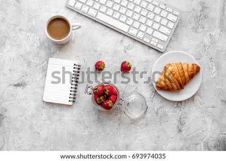Dessert fo light lunch at workplace. Coffee, strawberry, croissant near keyboard on grey background top view