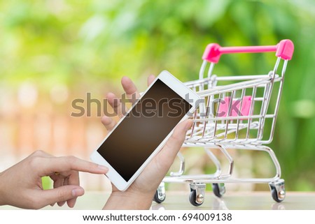 Woman hand holding mobile overt image of shopping cart with blurred green nature background,shopping online concept.
