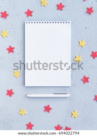 A notebook and a white pen are on a blue concrete background with red and yellow stars. There is an empty space for your text. Vertical image