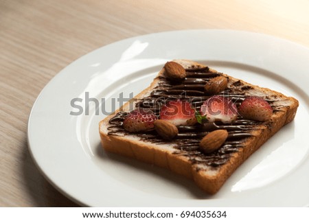 Natural lighting and shadow of blur ripe organic strawberry slice and almonds on bread slice with spread for breakfast on wooden kitchen bar. Healthy snack background with copy space.