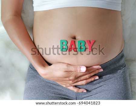 Close up Pregnant woman sitting on soft sofa and touching her belly with sign BABY in front of her belly.