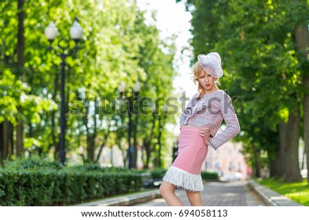 Portrait of a young blonde in a pink suit in a park outdoors. Vintage style