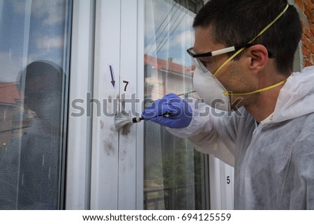 Male forensic expert find fingerprints on the window with help brush and black powder