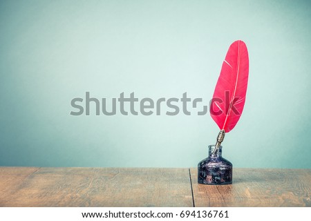 Vintage old red quill pen with inkwell on wooden table front gradient mint green wall background. Retro style filtered photo Royalty-Free Stock Photo #694136761