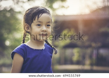 Asian cute little girl dressed in blue with a bright smile on his face. The backdrop is an old wooden house and the light of sunset.