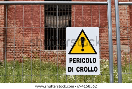 A yellow warning of danger to collapse in front of one buildings of the old damaged Cittadella of Alessandria, Italy.