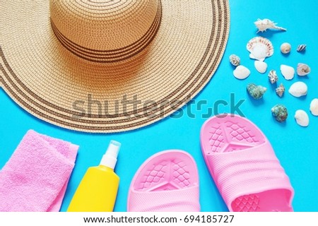 Straw hat, pink towel, yellow sunscreen bottle, slippers, seashells on a blue background. Flat lay beach background. Summer holiday concept. Many items