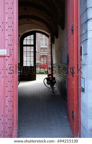 View into passageway in Bruges / Brugge, Belgium, with bicycle and red door. Photo taken summer 2017. Sign above internal doorway 'ingang' translates as 'entrance'.