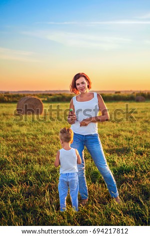 Mom and his little son went out for a walk in a field on which there are stacks of hay. Family walk in the field at sunset