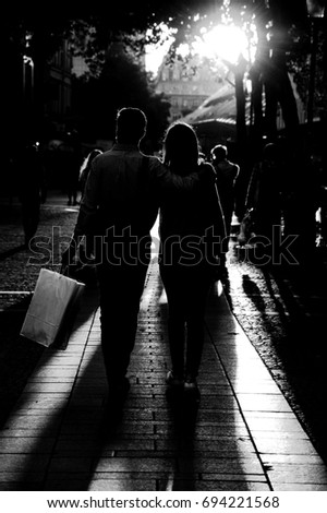 Couple after shopping walking at Parisian pedestrian street in golden sunset light. Back view. Paris (France). Black and white. High contrasting backlight.