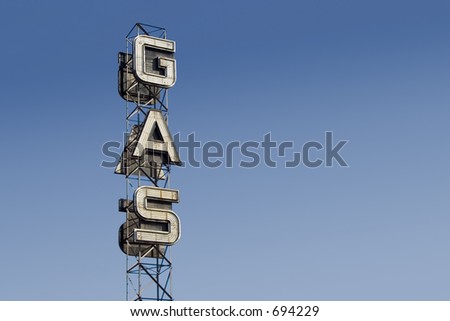 An industrial looking sign for a gas station against the blue sky.