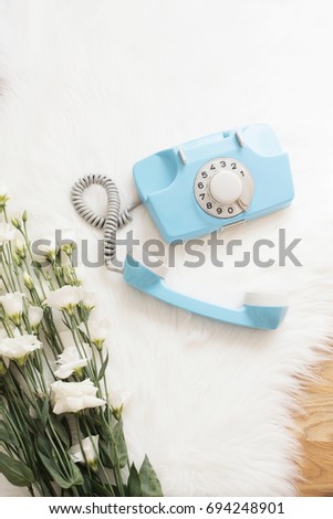A large bouquet white flowers and blue retro phone on wood floor on a white fur carpet. Cozy, fashion comfortable femininity home. Flat lay style. Top view, vertical image