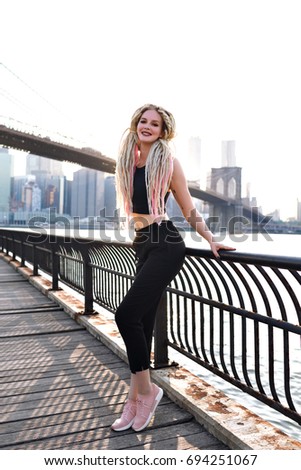 Young woman travel in usa , posing on New York, amazing view on Brooklyn bridge and manhattan island, stylish urban traveler, unusual dread blonde hairs, sportive body, america trip.