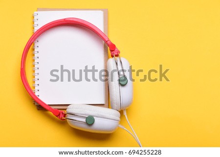 Headset for music and blank page with copy space. Headphones in white and red color with empty notebook. Music and note taking concept. Modern earphones isolated on yellow background, top view