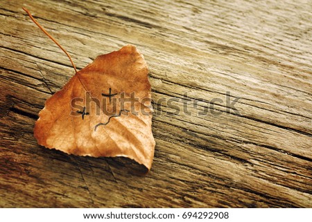 Brown dried  leaf with a picture of a sad face on the old wooden background with cracks