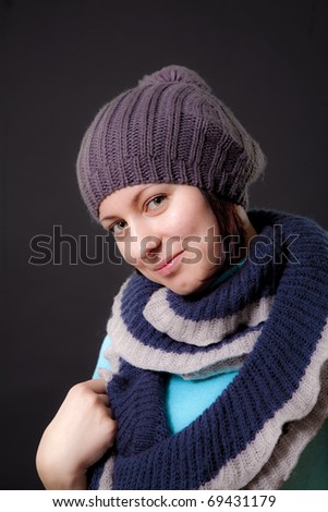 Portrait to the young woman in a cap with a scarf on a black background