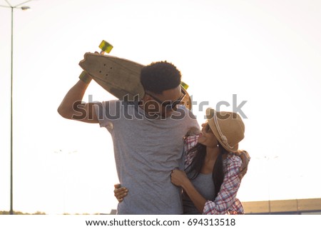 portrait of happy yong couple hug each other, boy and girl with skateboard in sunny day 