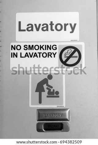 Black and white picture of No smoking message with prohibition sign and symbol of mother changing diaper for the baby on the vacant lavatory door on the plane