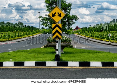 Beautiful asphalt road and two ways traffic sign with green trimmed plants in the park on white cloud and blue sky background