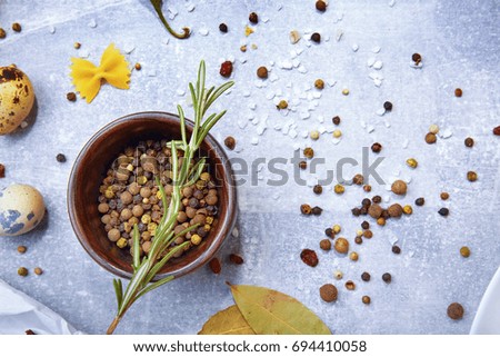 Macro picture of a brown wooden bowl with colorful seasoning on a gray background. Spices with quail eggs and a rosemary twig.
