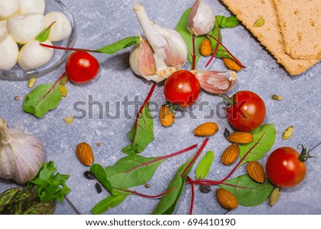 Macro picture of cherry tomatoes, green salad leaves, garlic and potatoes. Ingredients for summer salad on a gray background.