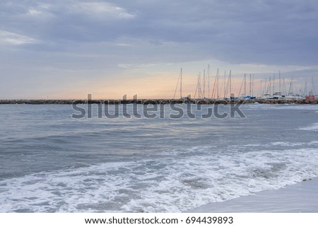 Beautiful sea landscape with waves in mild pink sunset romantic light with sailing boats on the background