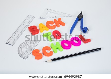 Back to school written with colourful alphabet learning letters alongside a pencil, protractor, ruler and geometry equipment on a plain white background with copy space.