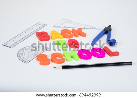 Back to school written with colourful alphabet learning letters alongside a pencil, protractor, ruler and geometry supplies on a plain white background with copy space.