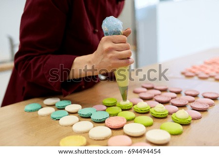 cooking, food and baking concept - chef with confectionery bag squeezing cream filling to macarons shells at pastry shop Royalty-Free Stock Photo #694494454